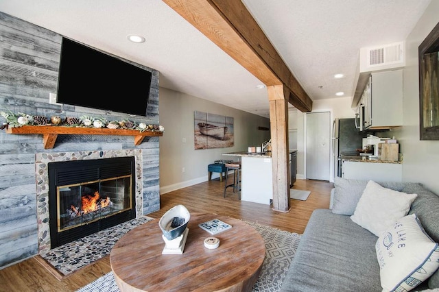 living room with wood-type flooring, beam ceiling, and a stone fireplace