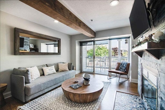 living room featuring a textured ceiling, dark hardwood / wood-style flooring, a stone fireplace, and beamed ceiling