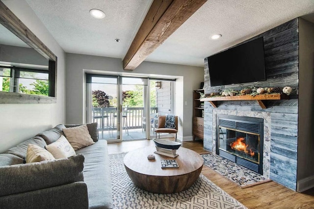 living room with hardwood / wood-style floors, a textured ceiling, beam ceiling, and a stone fireplace