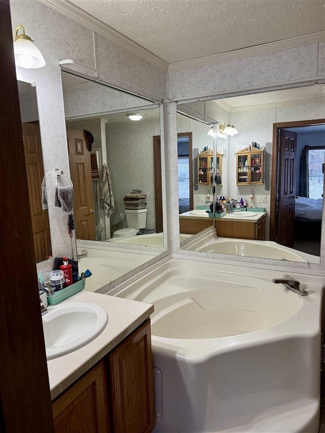 bathroom with a tub to relax in, vanity, toilet, crown molding, and a textured ceiling