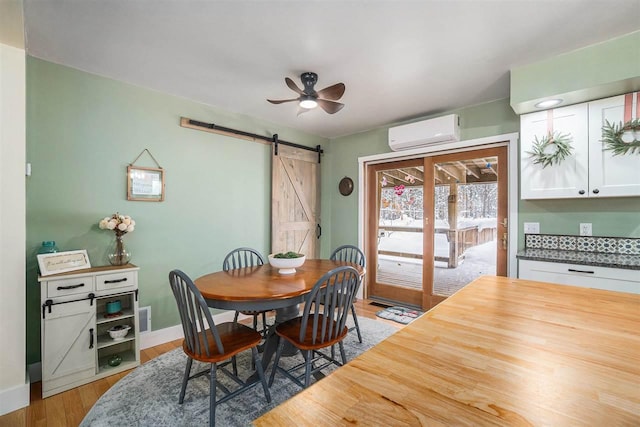 dining area featuring ceiling fan, a wall unit AC, a barn door, and light wood-type flooring