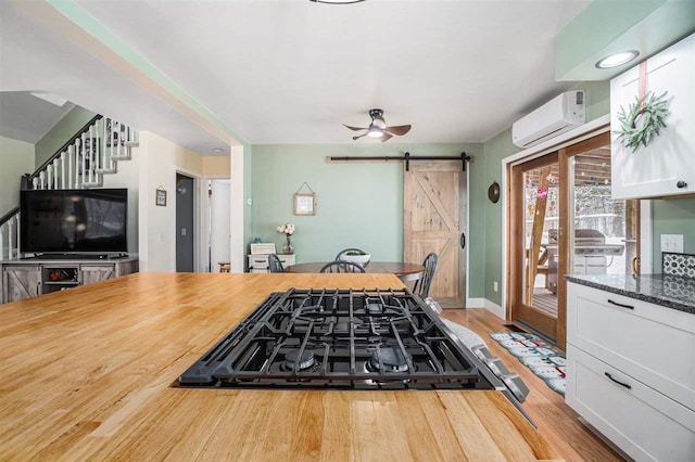 kitchen featuring white cabinetry, a barn door, a wall mounted air conditioner, stovetop, and light hardwood / wood-style floors