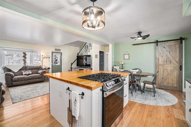 kitchen featuring butcher block counters, a barn door, white cabinets, light wood-type flooring, and stainless steel range with gas cooktop