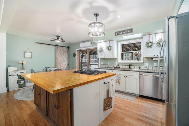 kitchen featuring a center island, white cabinetry, a barn door, hanging light fixtures, and stainless steel appliances