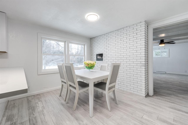 dining area with ceiling fan, brick wall, and light wood-type flooring