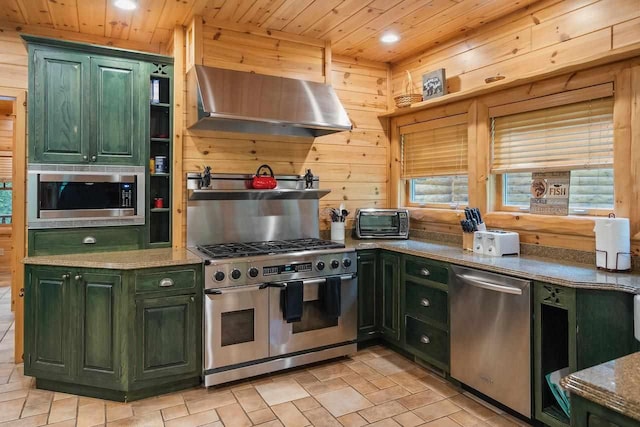 kitchen with appliances with stainless steel finishes, exhaust hood, green cabinets, and wood walls