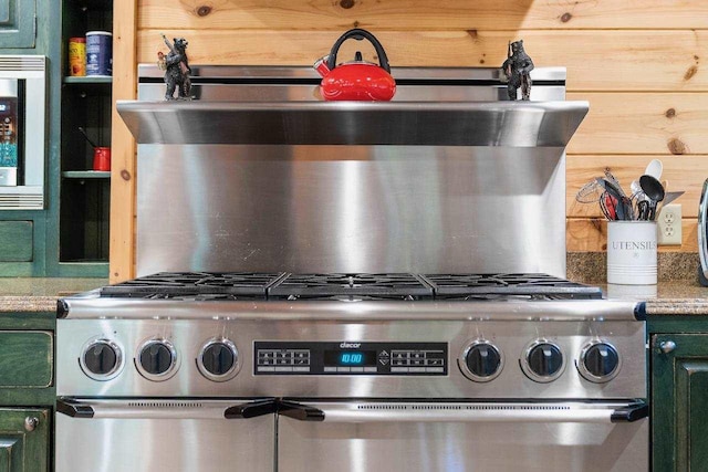 details featuring high end stainless steel range oven, stone counters, green cabinets, wine cooler, and wood walls