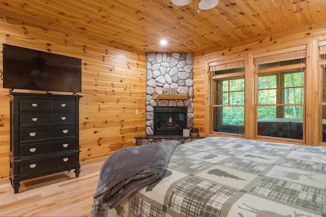 bedroom with wood ceiling, wooden walls, a stone fireplace, and light hardwood / wood-style flooring