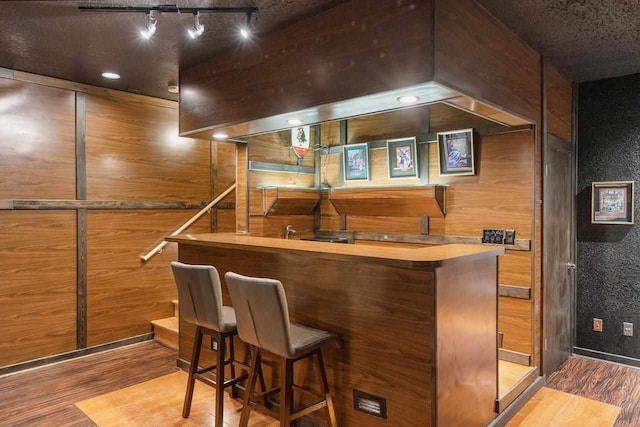 bar featuring track lighting, hardwood / wood-style floors, and wood walls