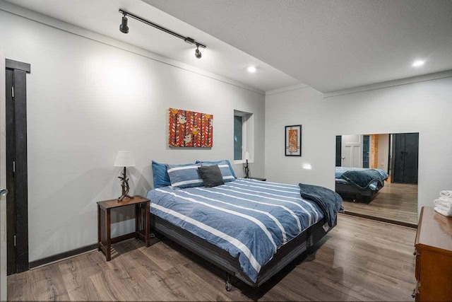 bedroom with hardwood / wood-style floors, ornamental molding, and rail lighting