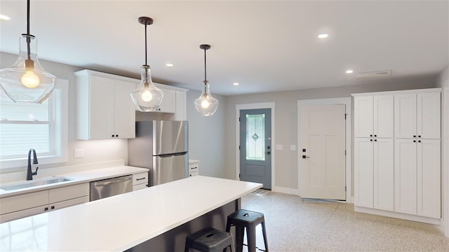 kitchen with a kitchen bar, sink, appliances with stainless steel finishes, pendant lighting, and white cabinets