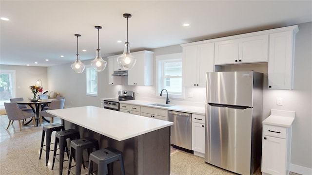 kitchen with sink, stainless steel appliances, a center island, white cabinets, and decorative light fixtures