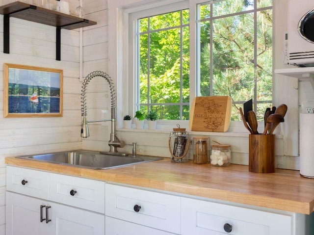 kitchen with white cabinetry, wooden walls, and sink