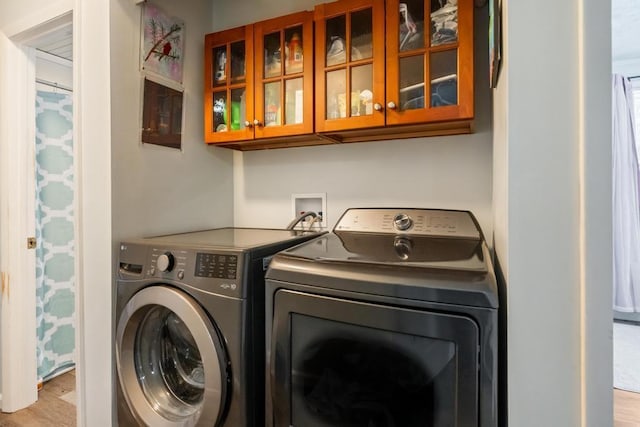 clothes washing area featuring cabinets, washing machine and clothes dryer, and light hardwood / wood-style flooring