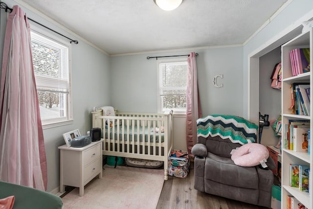 bedroom with a nursery area, ornamental molding, and light hardwood / wood-style floors