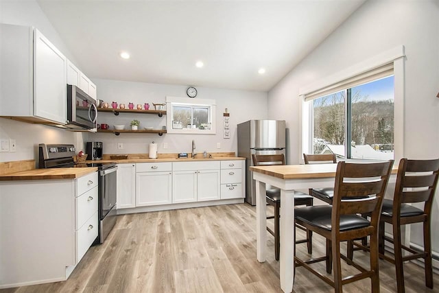 kitchen with appliances with stainless steel finishes, butcher block counters, sink, white cabinets, and light hardwood / wood-style flooring