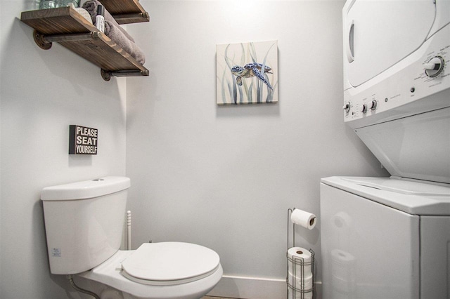 bathroom featuring stacked washer / drying machine and toilet