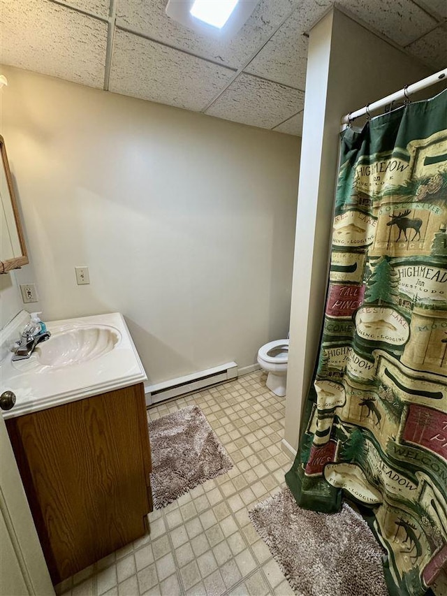 bathroom with baseboard heating, vanity, toilet, and a drop ceiling