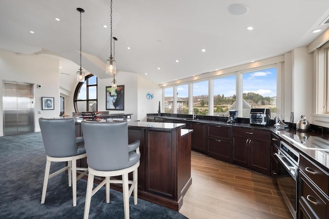 kitchen with a kitchen bar, hanging light fixtures, elevator, a kitchen island, and oven