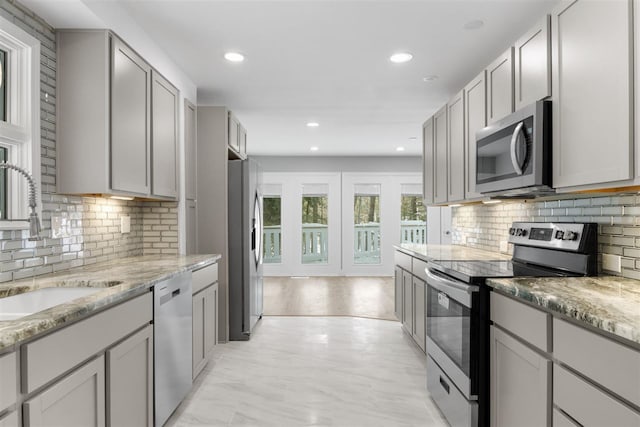 kitchen featuring stainless steel appliances, light stone countertops, sink, and gray cabinetry