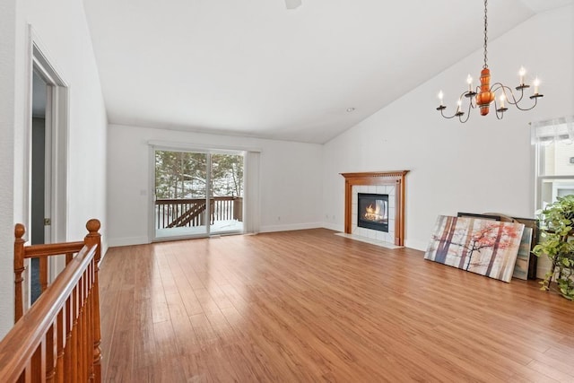 unfurnished living room with an inviting chandelier, lofted ceiling, a tiled fireplace, and light hardwood / wood-style floors