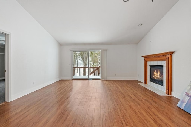 unfurnished living room featuring vaulted ceiling, a tile fireplace, and light hardwood / wood-style flooring