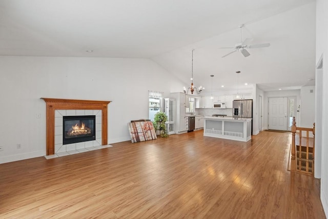 unfurnished living room with a tiled fireplace, high vaulted ceiling, ceiling fan with notable chandelier, and light hardwood / wood-style floors