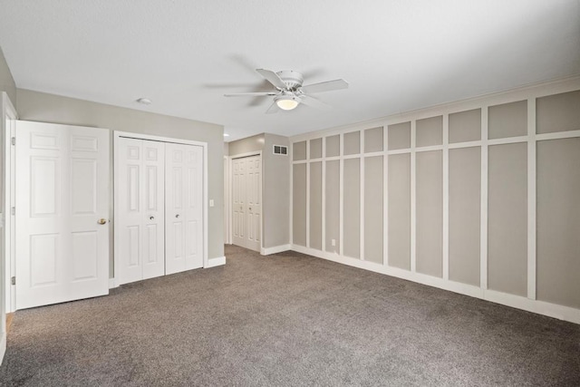 unfurnished bedroom with ceiling fan, two closets, and dark colored carpet