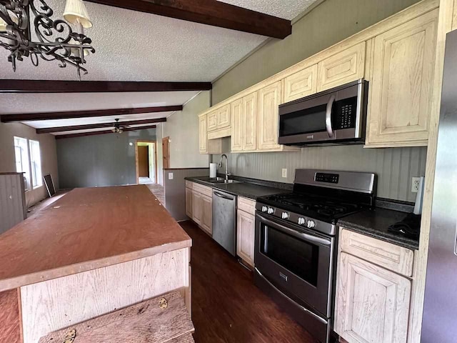 kitchen with sink, appliances with stainless steel finishes, cream cabinets, a textured ceiling, and beamed ceiling