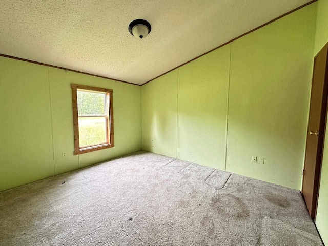 carpeted spare room featuring vaulted ceiling, ornamental molding, and a textured ceiling