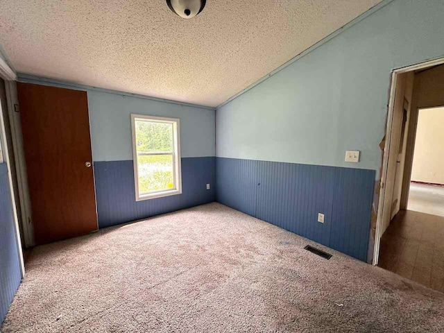 carpeted spare room with vaulted ceiling and a textured ceiling