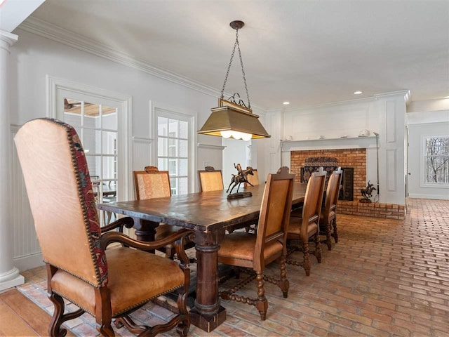 dining space with crown molding, a fireplace, and decorative columns