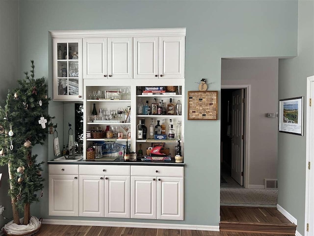 bar with white cabinetry and dark hardwood / wood-style flooring