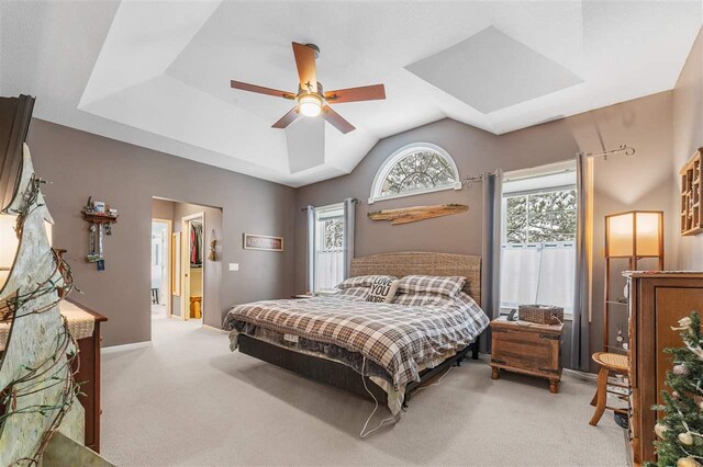 bedroom with ceiling fan, a tray ceiling, and light carpet