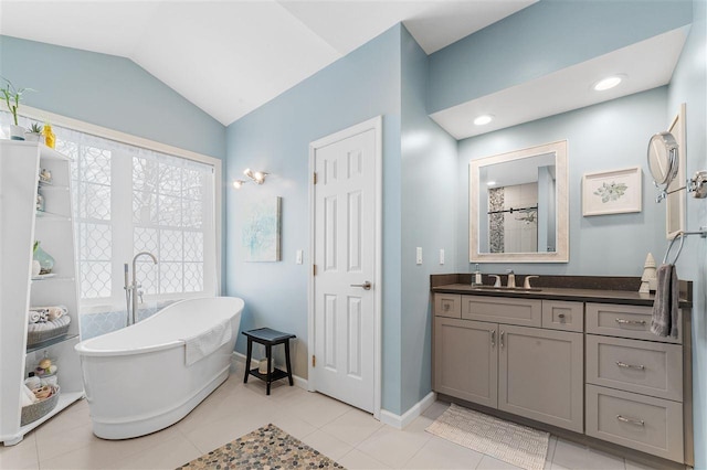 bathroom with tile patterned floors, lofted ceiling, a bathing tub, and vanity