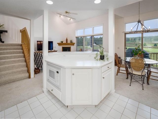 kitchen with white microwave, decorative light fixtures, white cabinets, a chandelier, and light carpet