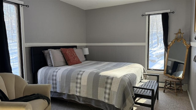 carpeted bedroom with a baseboard heating unit, multiple windows, and wainscoting