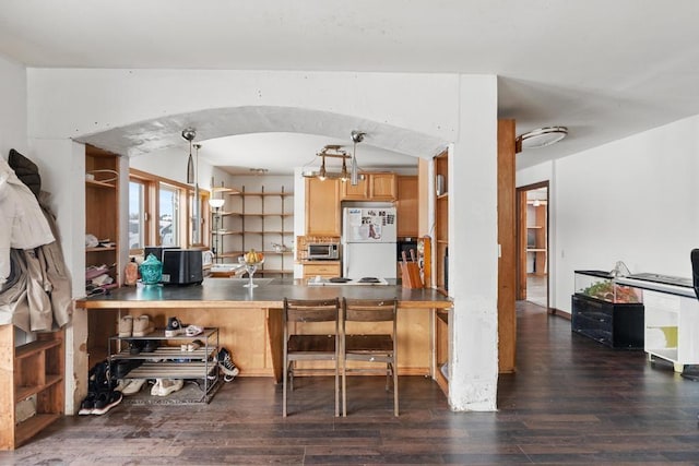 kitchen with white fridge, dark wood-type flooring, kitchen peninsula, and decorative light fixtures