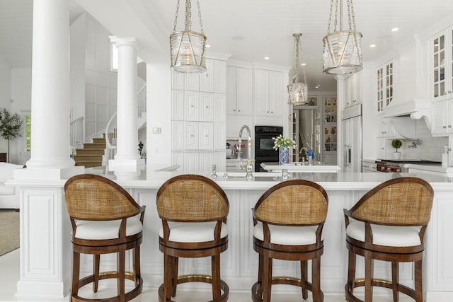 kitchen featuring decorative light fixtures, paneled built in fridge, decorative columns, and a center island with sink