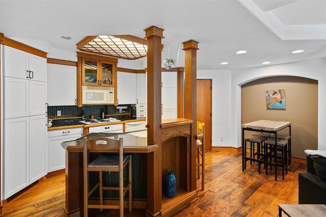 kitchen featuring white cabinetry, white appliances, a breakfast bar, and hardwood / wood-style flooring