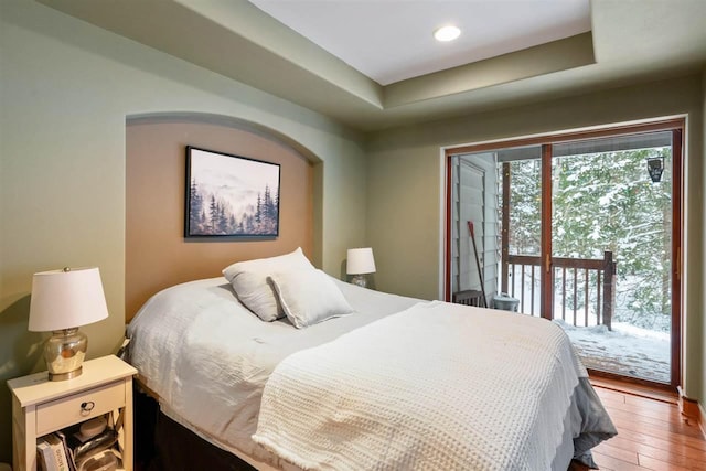 bedroom featuring a raised ceiling, wood-type flooring, and access to outside