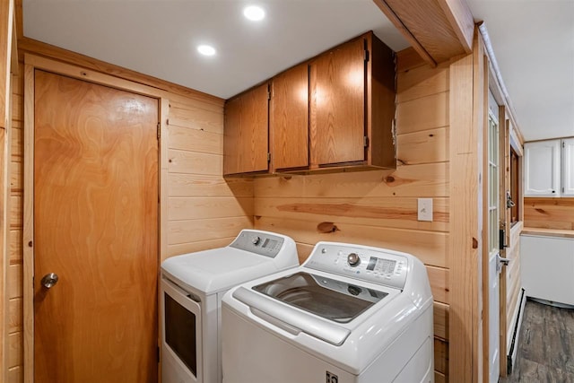 washroom with wood walls, dark hardwood / wood-style flooring, cabinets, a baseboard heating unit, and washing machine and clothes dryer