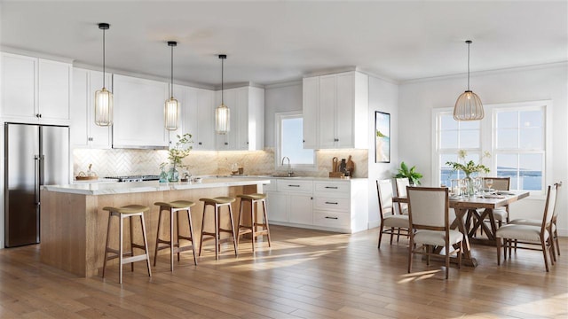 kitchen with white cabinetry, hardwood / wood-style floors, stainless steel built in refrigerator, a kitchen island, and decorative light fixtures