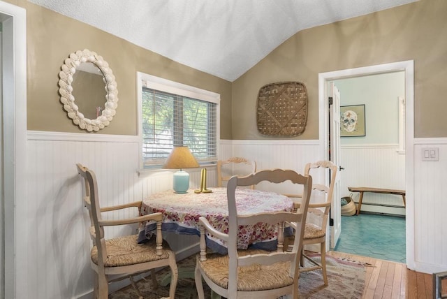 dining space featuring hardwood / wood-style flooring, vaulted ceiling, and a baseboard radiator