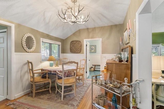 dining room featuring lofted ceiling, wood-type flooring, a textured ceiling, and a notable chandelier