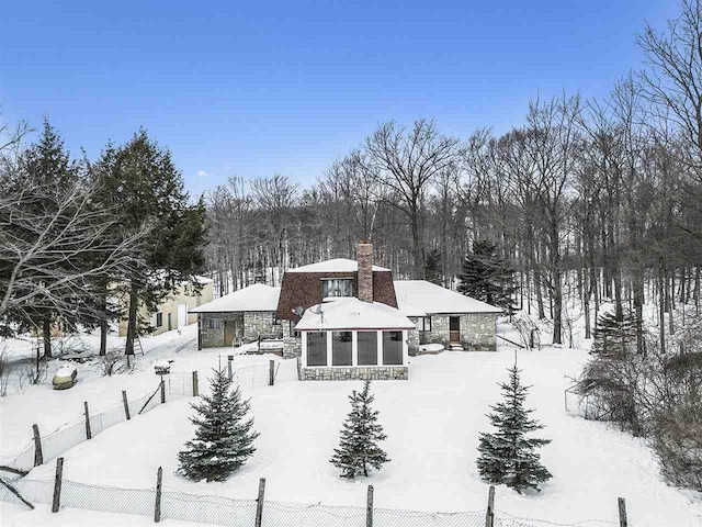 snow covered back of property with a sunroom