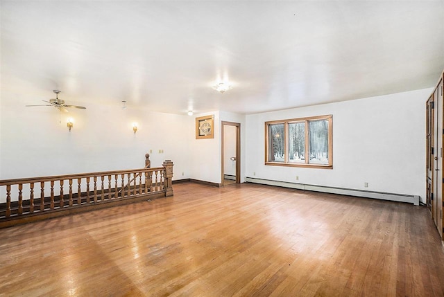 empty room featuring baseboard heating, ceiling fan, and light wood-type flooring