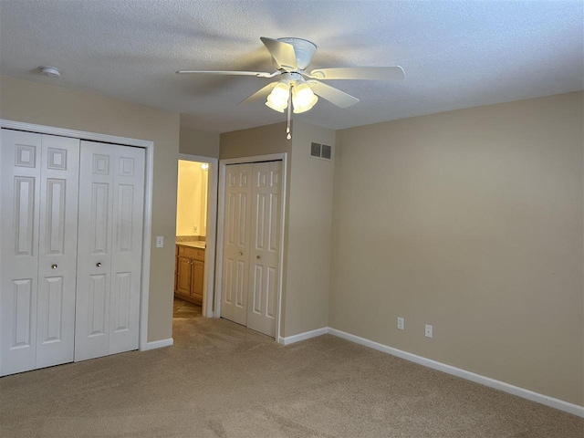 unfurnished bedroom with ceiling fan, light carpet, two closets, and a textured ceiling