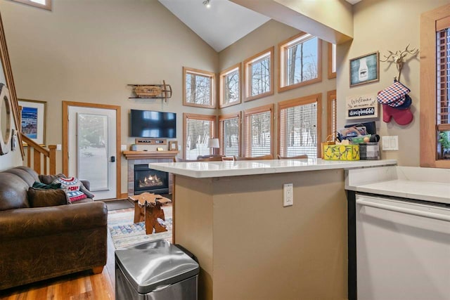 kitchen featuring dishwasher, high vaulted ceiling, a fireplace, kitchen peninsula, and light wood-type flooring