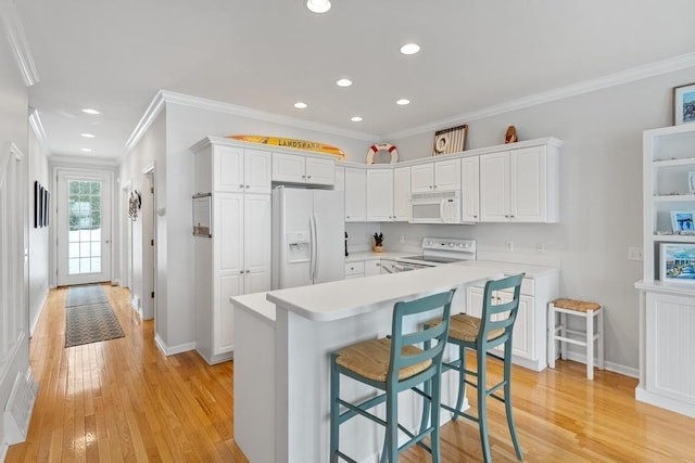 kitchen with white cabinetry, light wood finished floors, light countertops, white appliances, and a kitchen breakfast bar